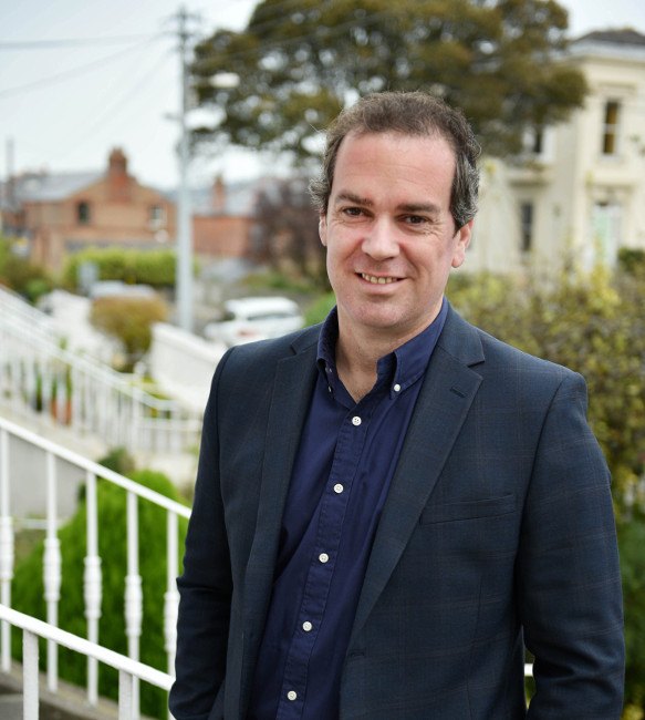 gavin carpenter outside on steps with houses and greenery in background