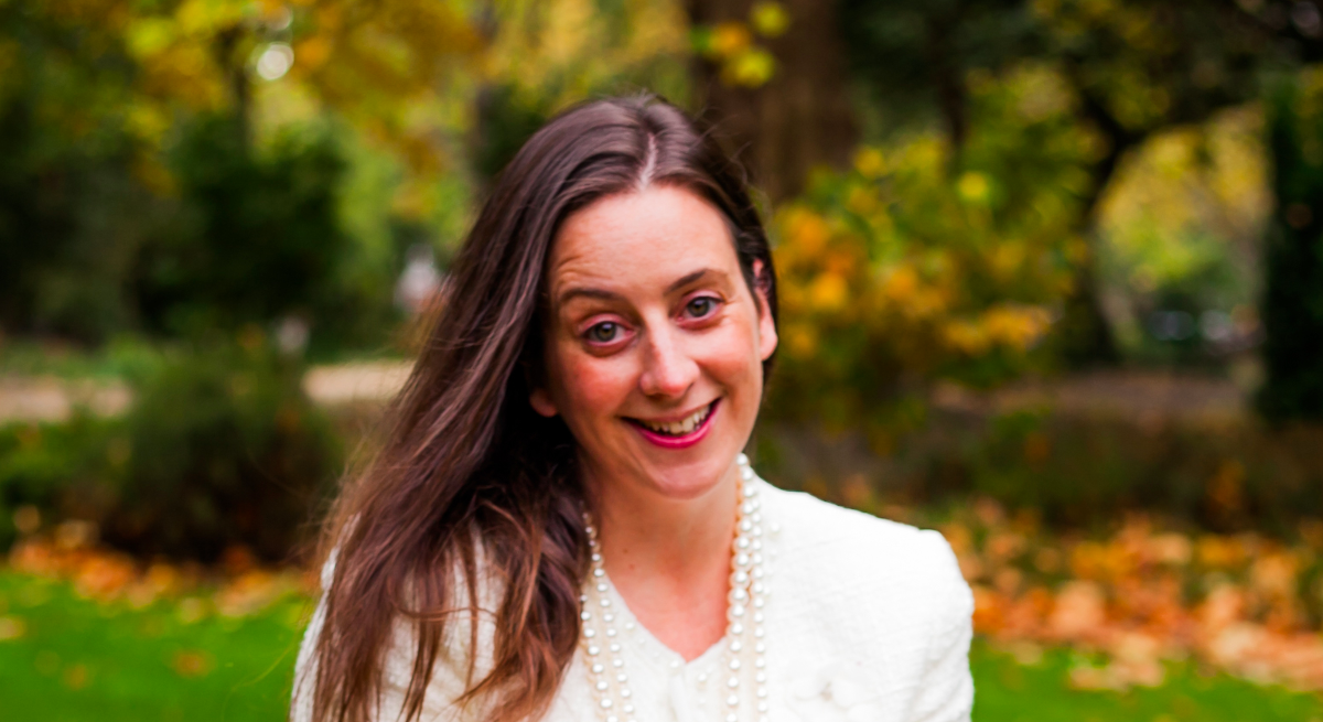 A headshot of Joanne Dolan sitting outside beneath autumnal trees.