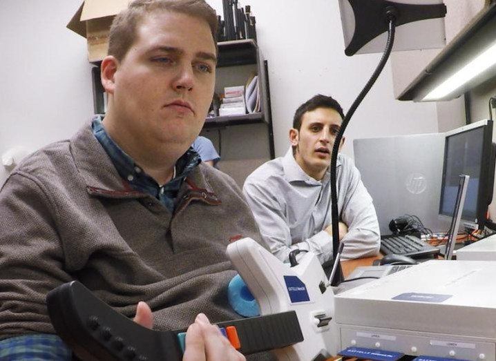 Battelle’s Nick Annetta (right) watches as Ian Burkhart plays a guitar video game using his paralyzed hand. Image: The Ohio State University Wexner Medical Center