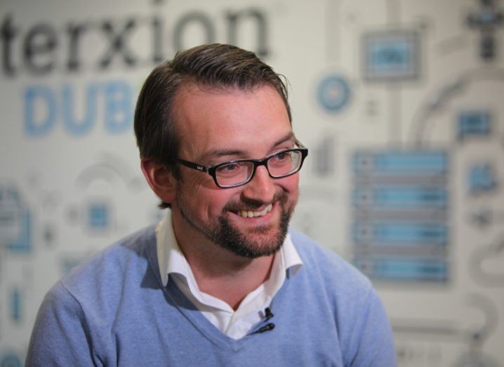 Man in blue jumper wearing glasses smiling.