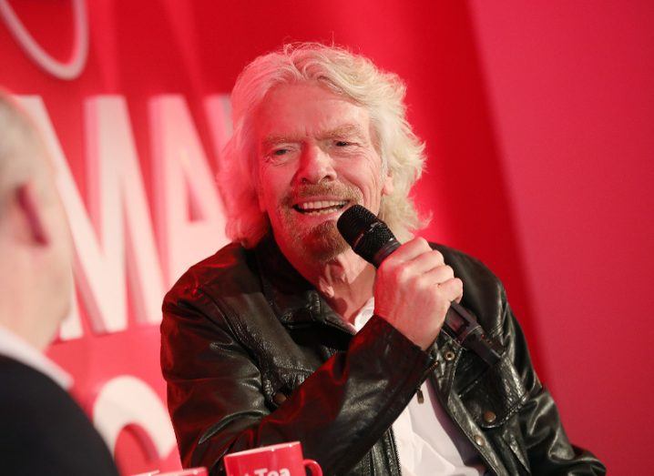 Richard Branson sits on a stage talking into a microphone.