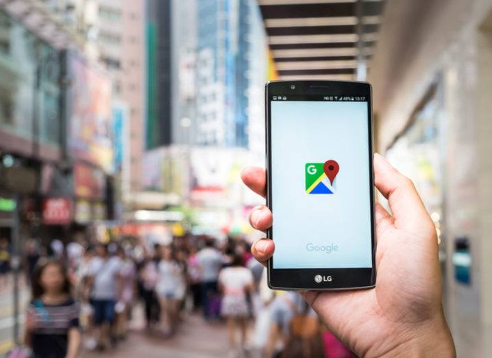 Hand holding an Android phone on a busy street in Hong Kong with Google Maps app open.