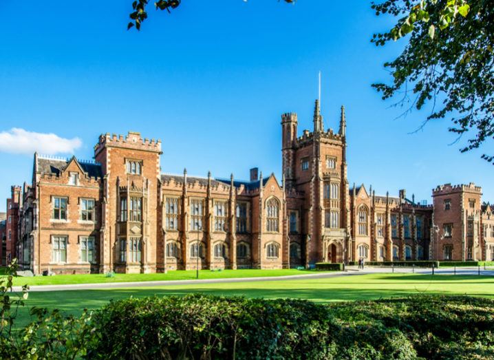 A backdrop of a clear-blue sky with a green lawn and the front of Queen's University Belfast.