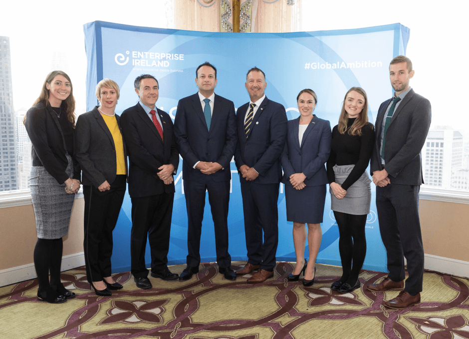 Leo Varadkar stands at the centre of a row of people in business attire, standing in front of an Enterprise Ireland backdrop.