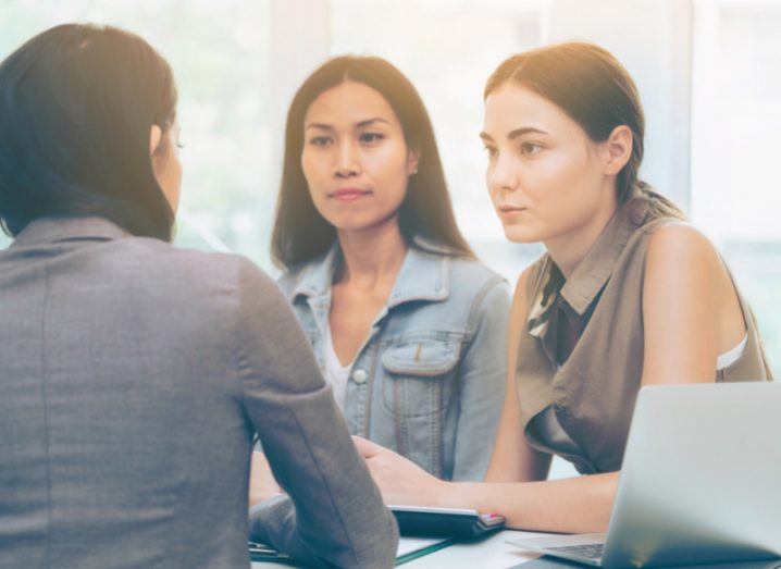 Three women speaking about strategy together at a table during a business meeting.