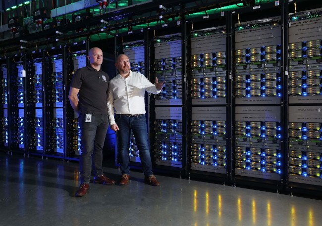 Two men stand beside clusters of servers in Facebook data centre.