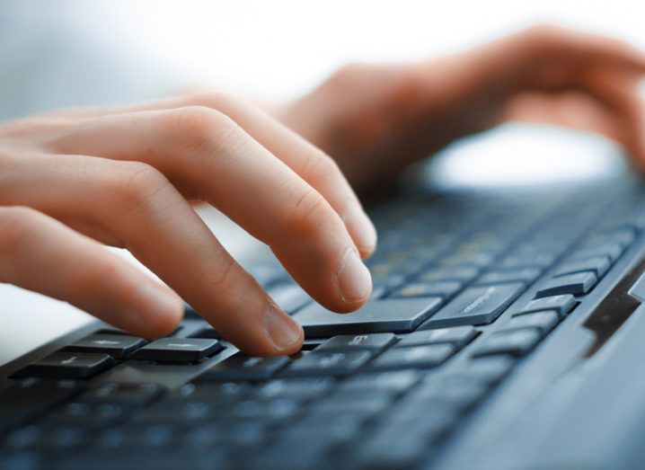 Close-up of a person's hands typing on a black keyboard.