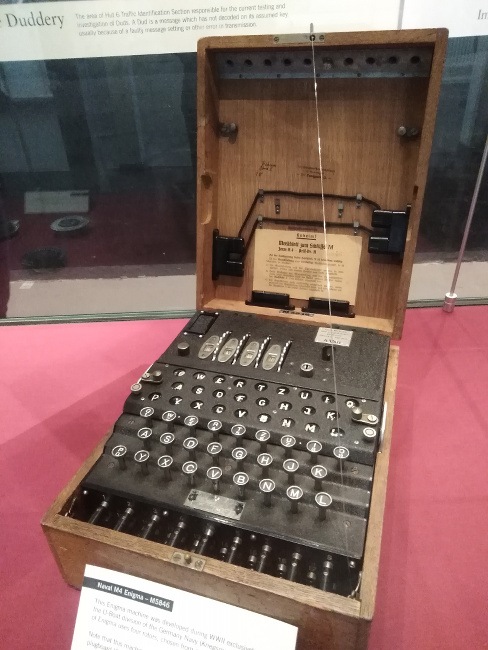An old machine that looks like a large typewriter in a wooden case is showcased in a museum exhibition.