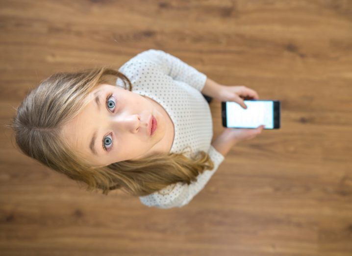 Little girl with blue eyes holding smartphone.