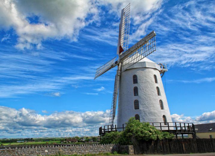 A white windmill stands before a vivid blue sky with clouds.