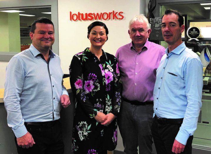 Three men and a woman stand in front of a LotusWorks sign.