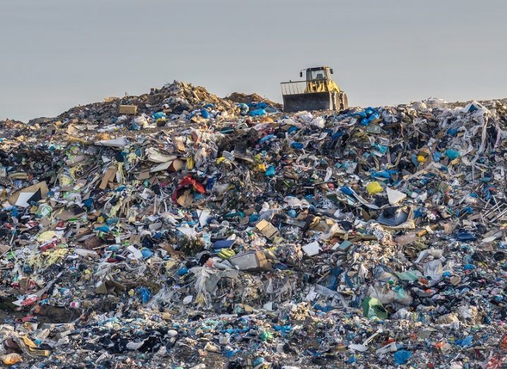 Bulldozer sitting on top of an enormous pile of plastic, taking up almost the entire image.