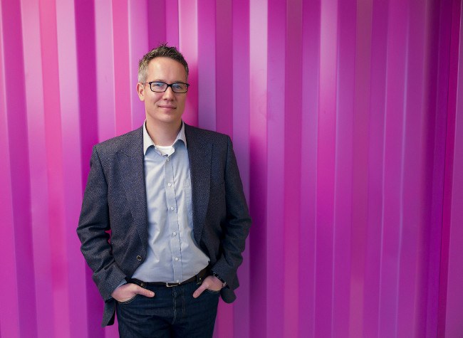 Man in grey jacket stands in front of pink metal wall.