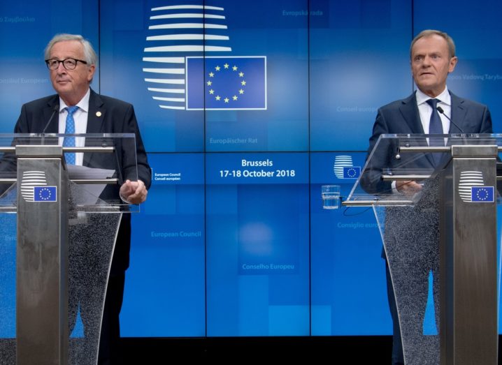 From left: Jean-Claude Juncker and Donald Tusk on stage at separate podiums with EU imagery in the background.