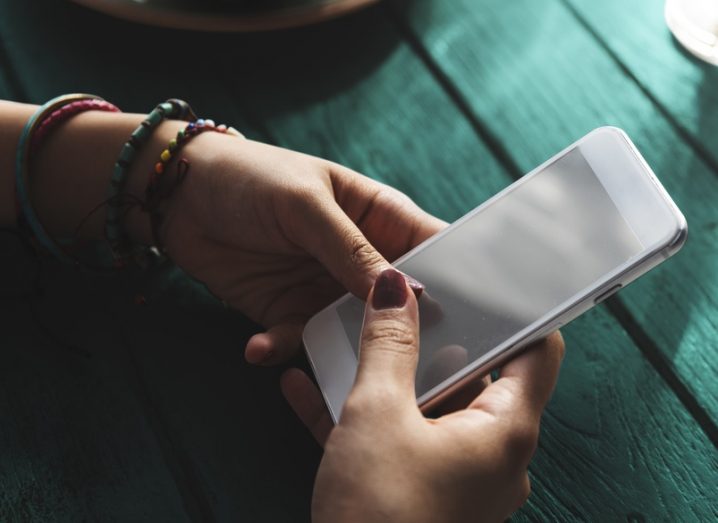 Woman using an iPhone, hands resting on a green wooden table.