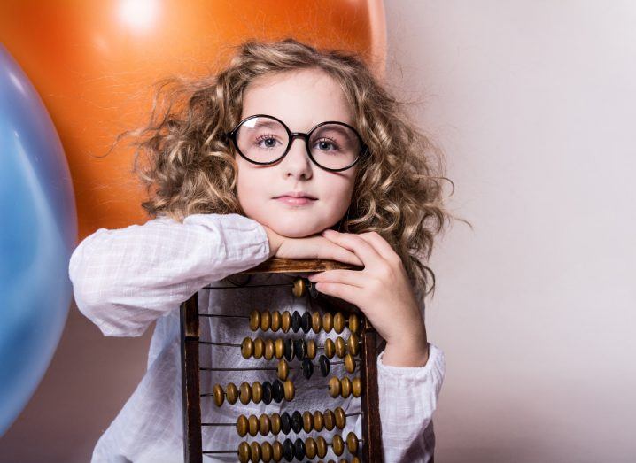 Girl with curly hair and glasses leans on an abacus.