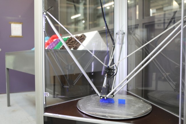 Looking inside a three-sided 3D printer through clear panels as it prints a plastic object.