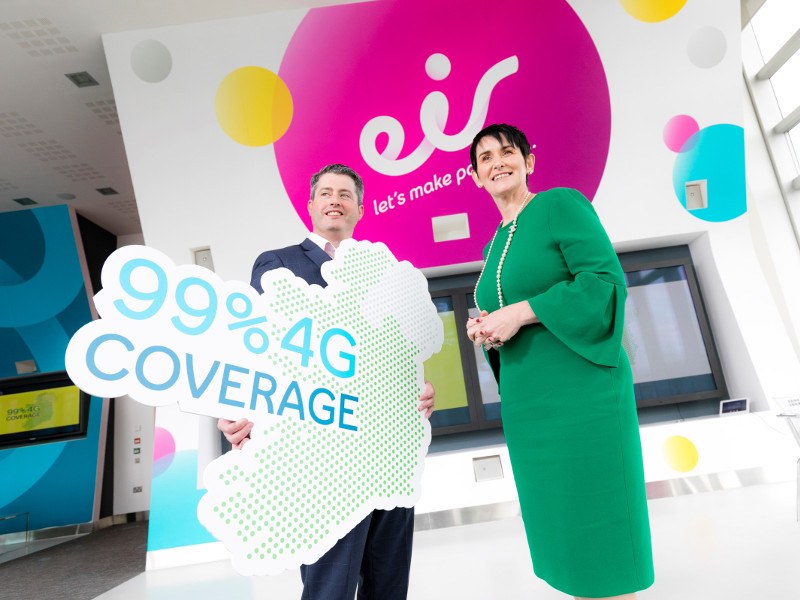 Man in suit with woman in green dress holding a sign saying 99 per cent 4G coverage.
