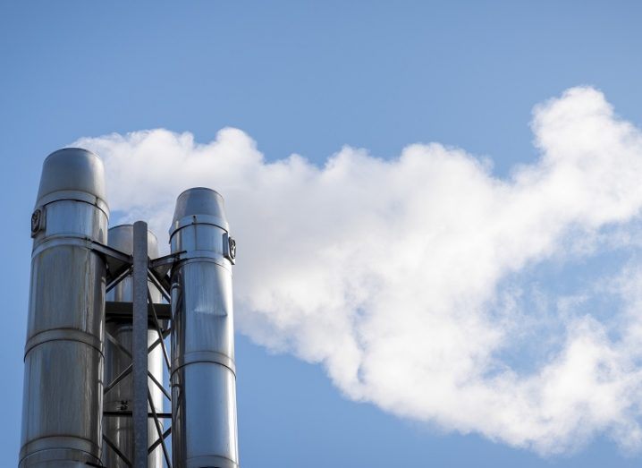 Smoke coming from a stack of multiple steel chimneys against a blue sky.