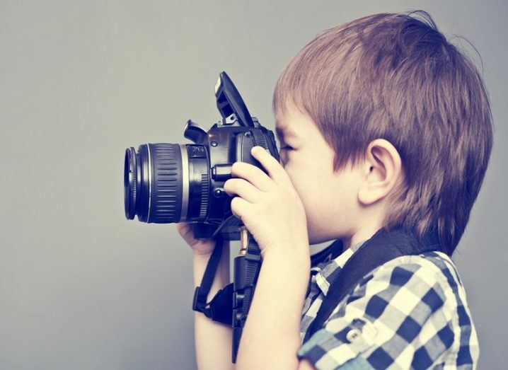 Small boy with brown hair facing left and taking a photo with a camera.