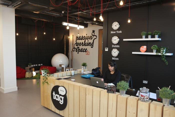 Chic co-working space reception area. The walls are black and there are plants around the reception desk.