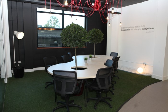 A meeting area with a curvy-shaped table with trees in the middle on a green carpet.