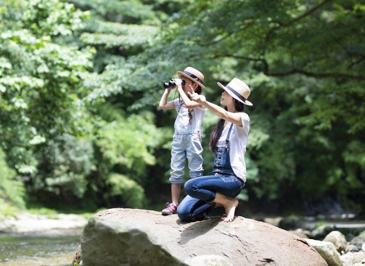 A woman and child are exploring a forest with binoculars.