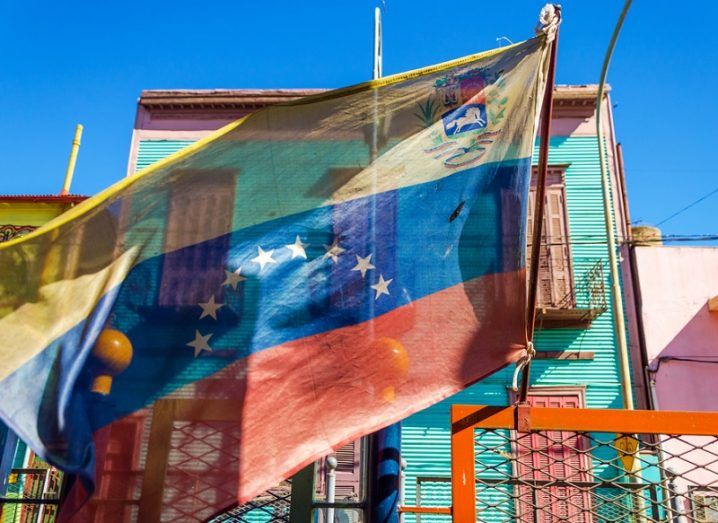 Venezuelan flag blowing in the wind with brightly coloured buildings.