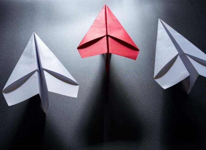 Three paper aeroplanes, two are white while the central one is pink. Marketing email symbol.