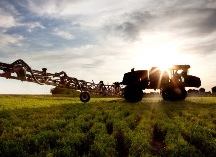 A silhouette of a high clearance sprayer on a field.