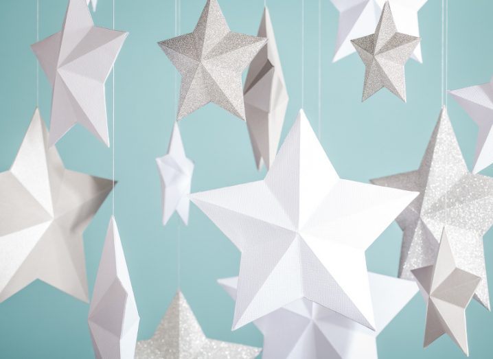 Hanging paper stars, some made from plain white card and others sparkling silver, against a light blue background.