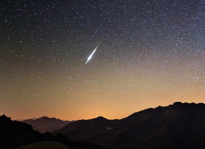 Comet shooting over a a sky with stars and a setting a sun.