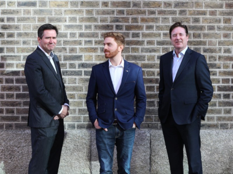 Three men in suits standing against a wall.