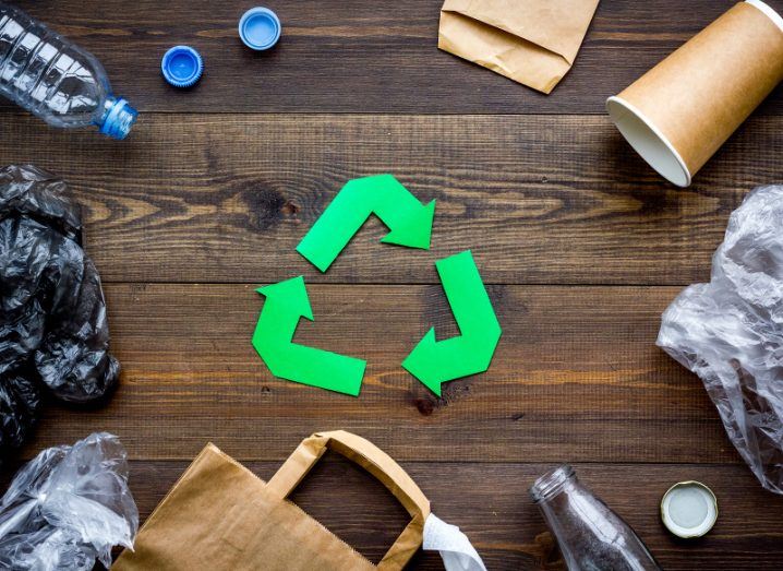 Discarded bags, bottles and disposable cups surround a paper cut-out recycling logo.