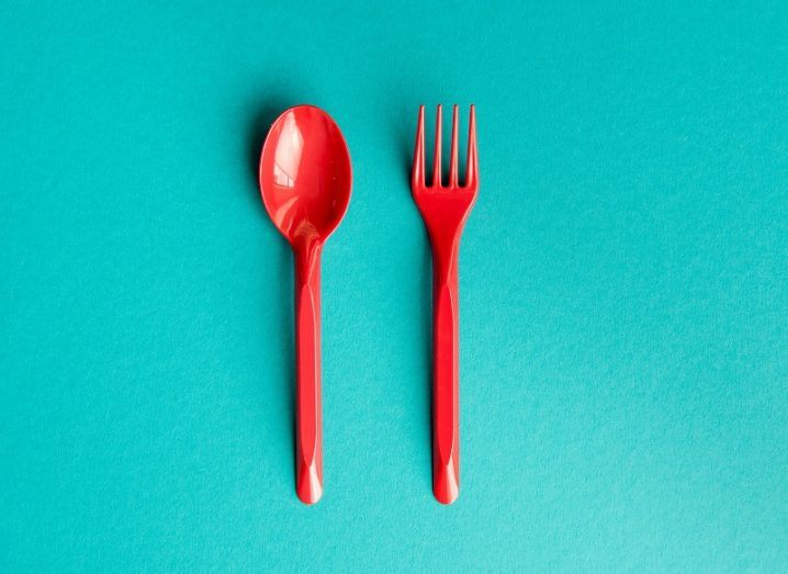 Bright red plastic fork and knife against a light blue background.