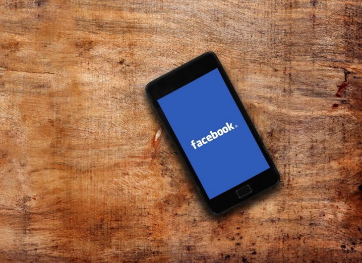 Facebook logo on display of a smartphone, resting on a wooden surface.