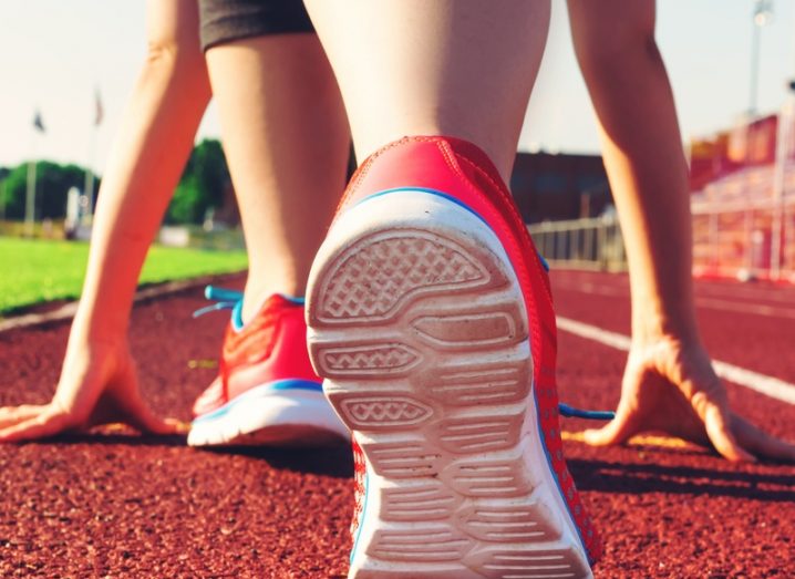 View of an athlete's running shoes and hands on a red track, preparing to race.