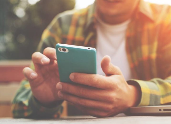 A man in a checked flannel shirt holding a smartphone in a blue protective cover.