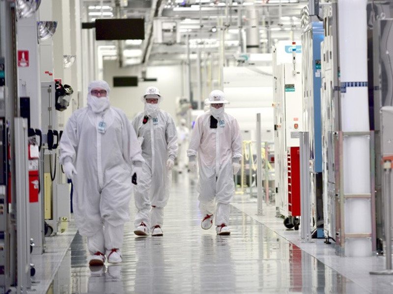 Intel workers in white clean room suits at a wafer fabrication facility.