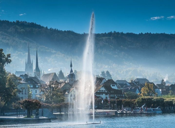 Old city of Zug, Canton Zug, Switzerland, with a water fountain shooting from lake to sky.