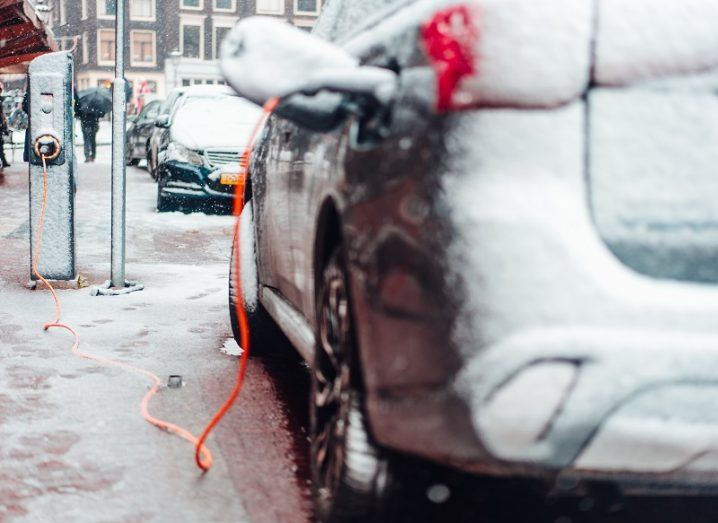 An EV parked on the side of a road covered in snow at a public charging point.