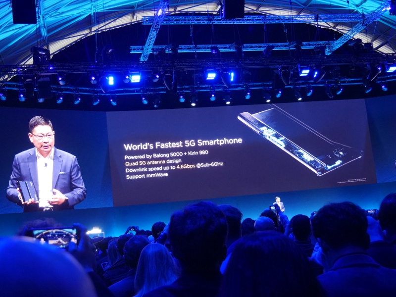 Man on stage at crowded tech event revealing specs to a new devices.