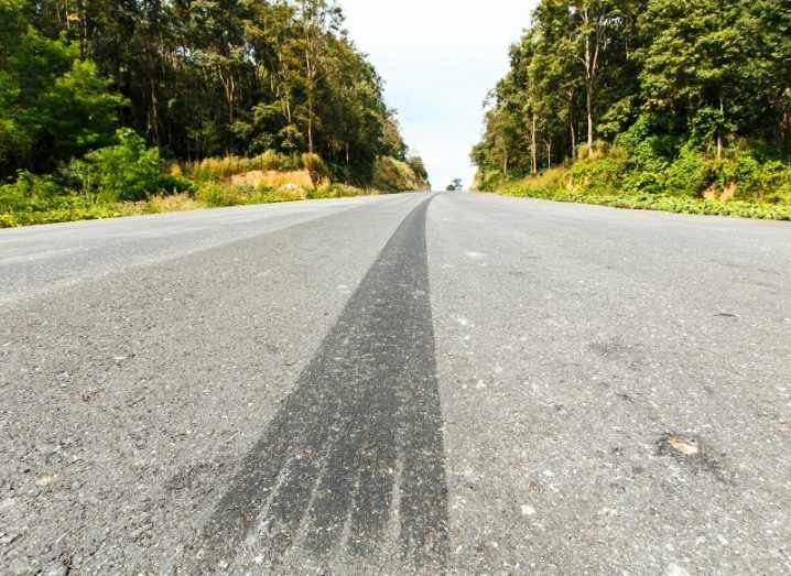 Tyre track carrying on into the distance on a tarmac road flanked by trees.