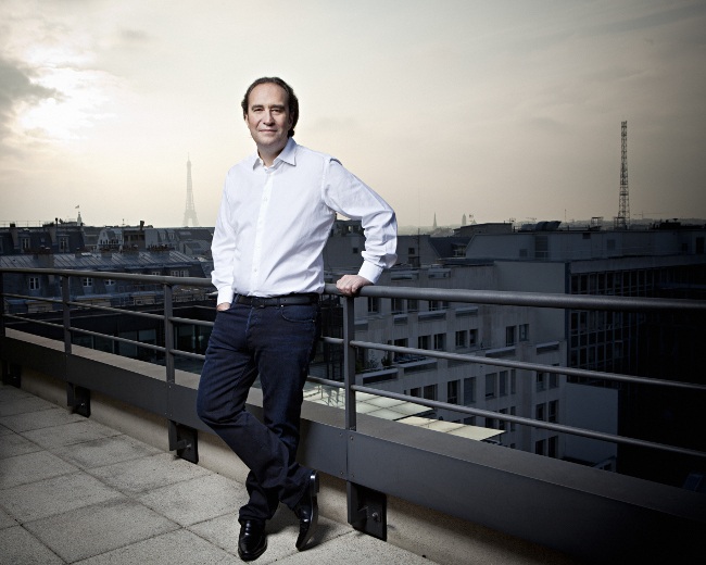 Man in white shirt standing on a balcony with Eiffel Tower in the background.