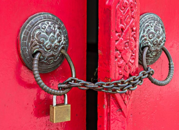 Red door with brass fittings locked using a chain and padlock, accessibility concept.