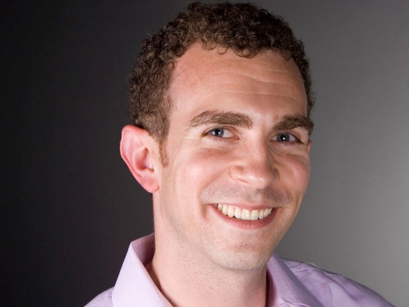 Smiling man with short curly hair in lilac shirt.