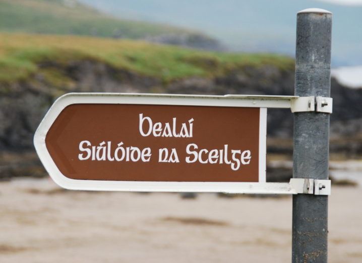 A signpost on a rocky beach reads ‘Bealaí Siúlóide na Sceilge’ in old Irish writing.