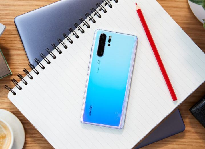 Picture of a blue-coloured Huawei P30 smartphone on a notebook beside a red pencil.