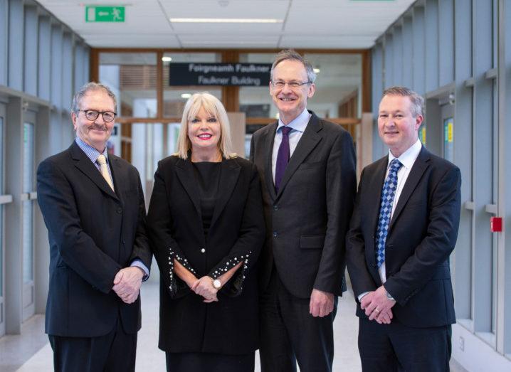 Three men in suits and one blonde woman in business dress standing in Dundalk IT and smiling.