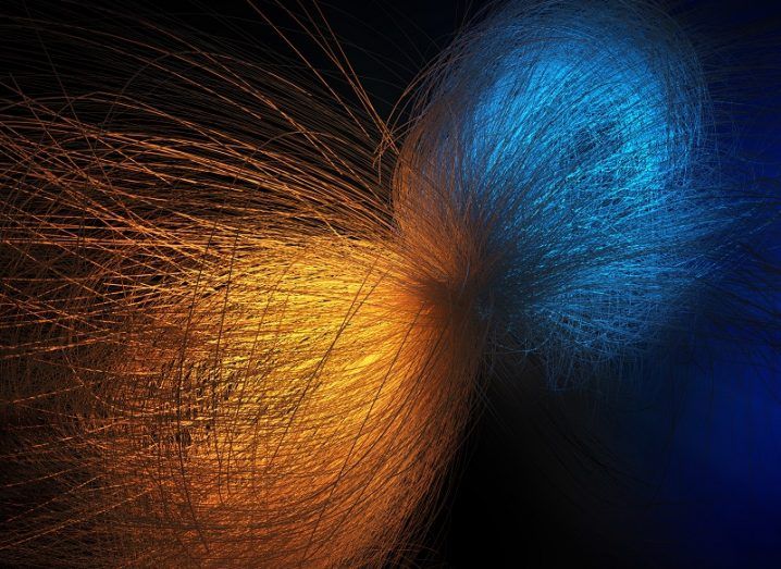 Abstract of two particles - one orange and one blue - colliding against a black background.